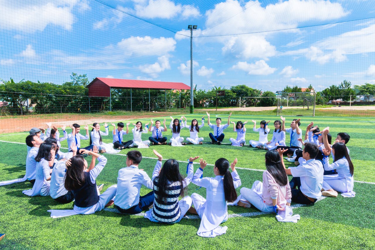 services-04 Students seated in a circle on a school field engaging in outdoor activities.