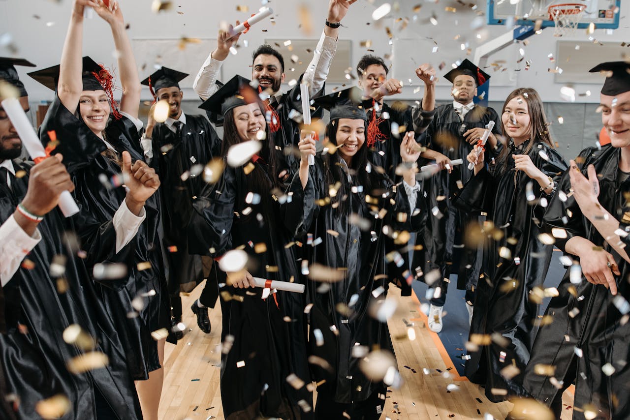 A diverse group of graduates celebrating with confetti indoors, capturing achievement and joy.